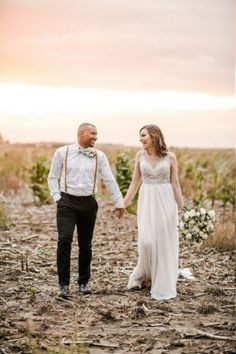 a bride and groom holding hands while standing in the middle of a field at sunset