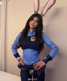 a woman in blue shirt and bunny ears standing next to a bed with her hands on her hips