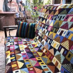 a multicolored blanket sitting on top of a couch next to a wooden chair