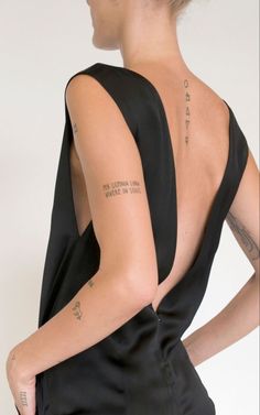 the back of a woman's black dress with tattoos on her left shoulder and right arm