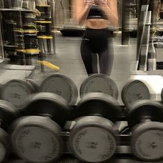 a woman taking a selfie in front of rows of dumbbells