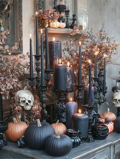 a table topped with lots of black candles and pumpkins next to a skull statue