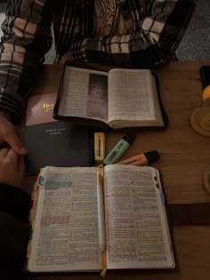 an open book sitting on top of a wooden table next to a person holding a pen