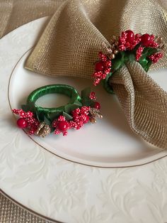 a white plate topped with a green ring and red berries on it next to a burlap napkin