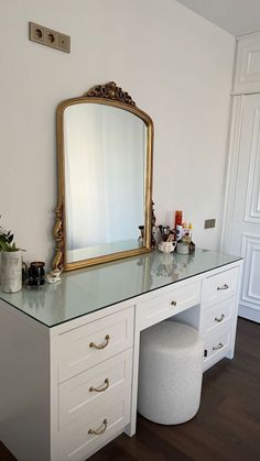 a vanity with a large mirror and stool in the corner, next to a white wall