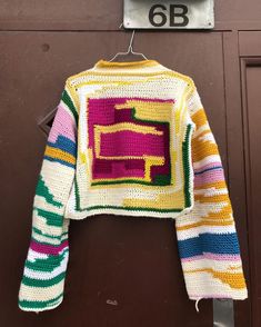 a crocheted sweater hanging on a door with the number 6b in it