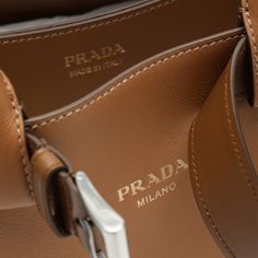 Caramel-coloured leather Prada medium bag featuring a decorative buckle belt, two top handles with strap detail, adjustable and removable shoulder strap, two internal compartments and contrasting front lettering logo. Width 33 cm x Height 22 cm x Depth 12 cm Adjustable shoulder strap length min 90 cm - max 100 cm Handle drop: 13 cm Size Type: INTMaterial: LeatherSKU: 1BA434OBO2CY9/O_PRADA-F03BH_100 Our Products Are 100% Genuine. In All Cases We Stand By The Authenticity Of Every Product Sold On Brown Prada Bag, Luxury Orange Shoulder Bag With Double Handle, Prada Arqué Leather Shoulder Bag, Tan Prada Bag, Orange Prada Bag, Balenciaga Backpack, Buckle Bag, Belt Women, Medium Bag