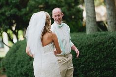 a man and woman standing next to each other in front of some bushes with trees