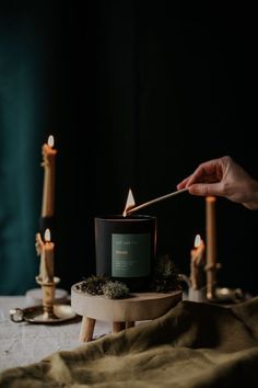 a person lighting a candle on a table with candles around it and other items nearby