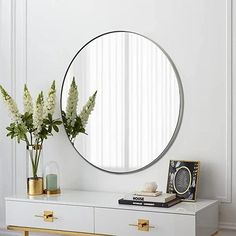 a round mirror on the wall above a dresser and vase with flowers in front of it