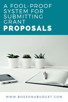 an open book sitting on top of a white table next to two potted plants