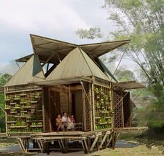 two people sit on the porch of a house made out of crates and bamboo sticks