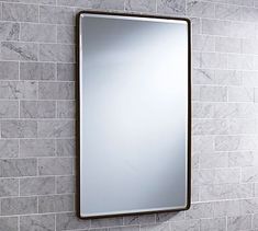 a bathroom mirror mounted to the side of a white tiled wall next to a sink