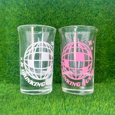 two drinking glasses with pink and white designs on them sitting in the grass next to each other