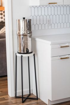 a tall metal container sitting on top of a wooden stand next to a kitchen counter