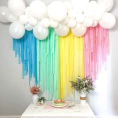 a table topped with balloons and cake next to a rainbow wall hanging from the ceiling