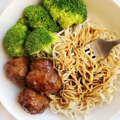 a white bowl filled with meatballs and noodles next to broccoli on a table