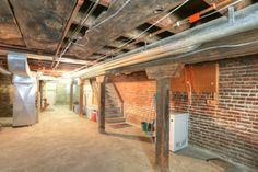 an unfinished room with exposed pipes and brick walls, including a spiral staircase leading up to the second floor