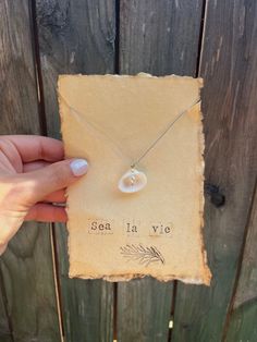 a person holding up an old piece of paper with a small shell on it and the word sea la vie written in cursive