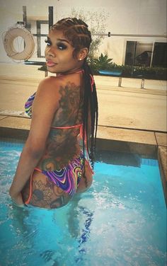 a woman in a pool with tattoos on her back and arms, wearing a colorful swimsuit