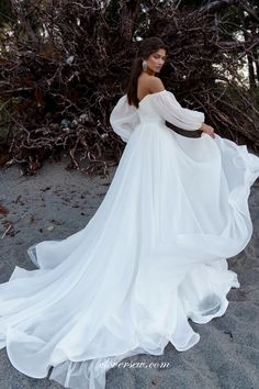 a woman in a white dress is standing on the beach with her arms behind her back