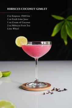 a pink drink in a coupe glass with limes and spices around it on a white table