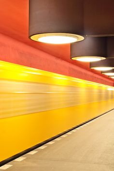 a long yellow and red train traveling through a subway station with lights on the ceiling