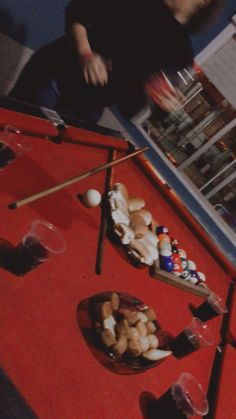 a man sitting at a pool table with several different items on the red cloth around him