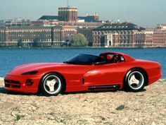 a red sports car sitting on top of a sandy beach next to the ocean with buildings in the background