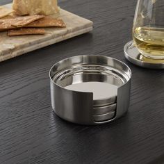 a metal container sitting on top of a wooden table next to a glass of wine