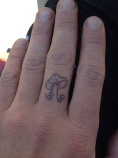 a person's hand with a small mushroom tattoo on the middle finger and an arrow in the middle