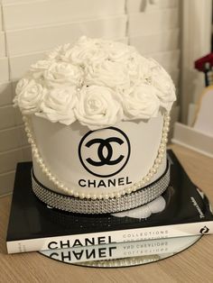 a chanel cake with white roses and pearls on top, sitting on a stack of books