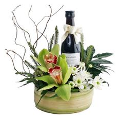 a bottle of wine sitting on top of a wooden container filled with flowers and greenery