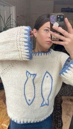 a woman taking a selfie in front of a mirror wearing a sweater with fish drawn on it