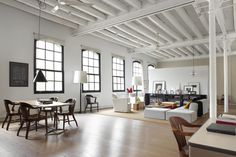 an open living room and dining area with white walls, wood floors and exposed ceilings