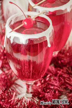 two glasses filled with liquid and cherries on top of red tinseled tinsel