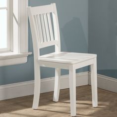 a white chair sitting in front of a window next to a wooden floor and blue wall