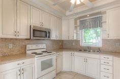 an empty kitchen with white cabinets and marble counter tops, including a stove top oven