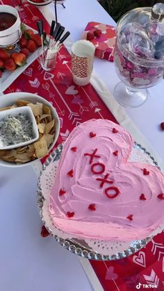 a heart shaped cake sitting on top of a table next to bowls of fruit and dips