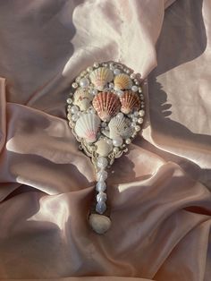 a brooch with seashells and pearls is laying on a pink satin sheet