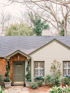 a small house with green shutters on the front door and windows that have plants growing out of them