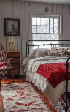 a bed sitting in a bedroom next to a wooden dresser and window with two candles on top of it