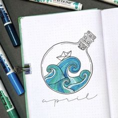 an open notebook with a drawing of a ship in a bottle on the cover and some markers next to it