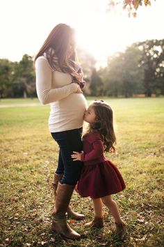 a pregnant woman is kissing her daughter's cheek while standing in the grass at sunset