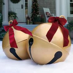 two gold christmas balls with red bows on them sitting in the snow near a house