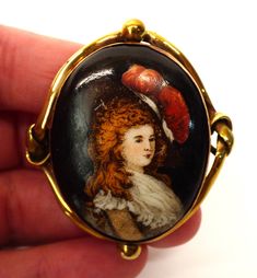 A gorgeous antique Victorian porcelain portrait brooch pin, probably continental. With an ornate gold plated mount, with a lovers knot either side, the central porcelain plaque is decorated with a bougie and flamboyant young woman wearing period dress with a scarlet coloured ostrich feather on her hat. A beautiful and fun piece, with a decadence and sass because of the dark background, not the ususal twee portraiture of the time. In nice vintage condition, some light marks to the surface under c Victorian Baroque Brooches As Gifts, Victorian Brooches For Ceremonial Occasions, Handmade Victorian Oval Brooches, Victorian Brooches For Vintage Events, Vintage Baroque Brooches As Gifts, Vintage Baroque Brooches For Gifts, Handmade Victorian Brooches For Ceremonial Use, Victorian Cabochon Brooch For Collectible, Antique Handmade Brooches For Formal Occasions