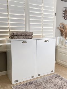 a white cabinet sitting next to a window with shutters on the side and a rug in front of it