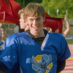 a young man wearing a blue jersey standing in front of other people at a football game