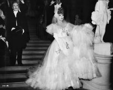 an old black and white photo of two women in evening dresses walking down the stairs