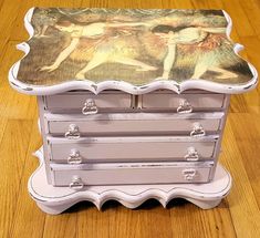 an old dresser with a painting on it's top sitting on a wooden floor